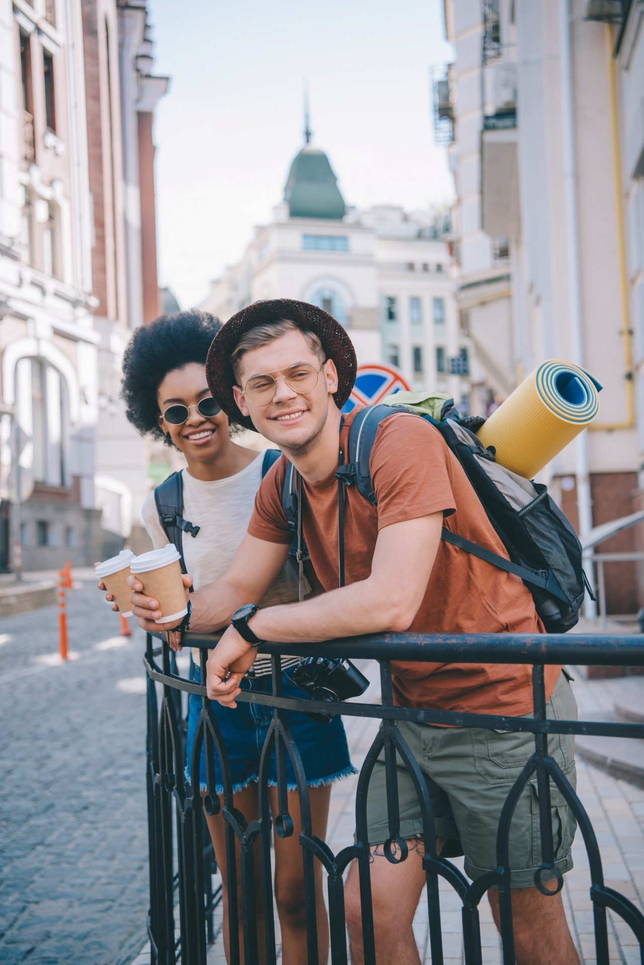 happy young interracial couple of travelers with paper cups of coffee.jpg